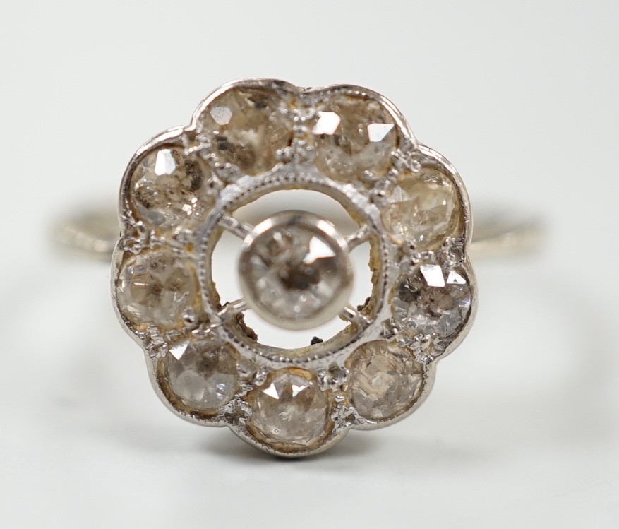 A 1920's white metal and ten stone millegrain set diamond flower head cluster ring, size P/Q, gross weight 3 grams.